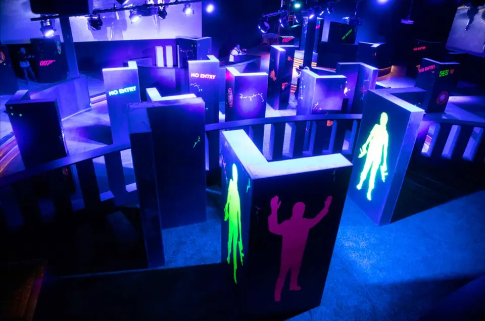 Lasergame-arena bij Bart & Bites van bovenaf: doolhof van wanden met neon-silhouetten in paars licht