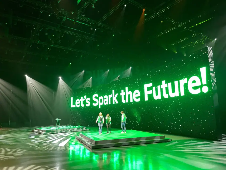 KPN-event in Barneveld: drie presentatoren op een podium voor een LED-wand met "Let's Spark the Future!" in groen licht