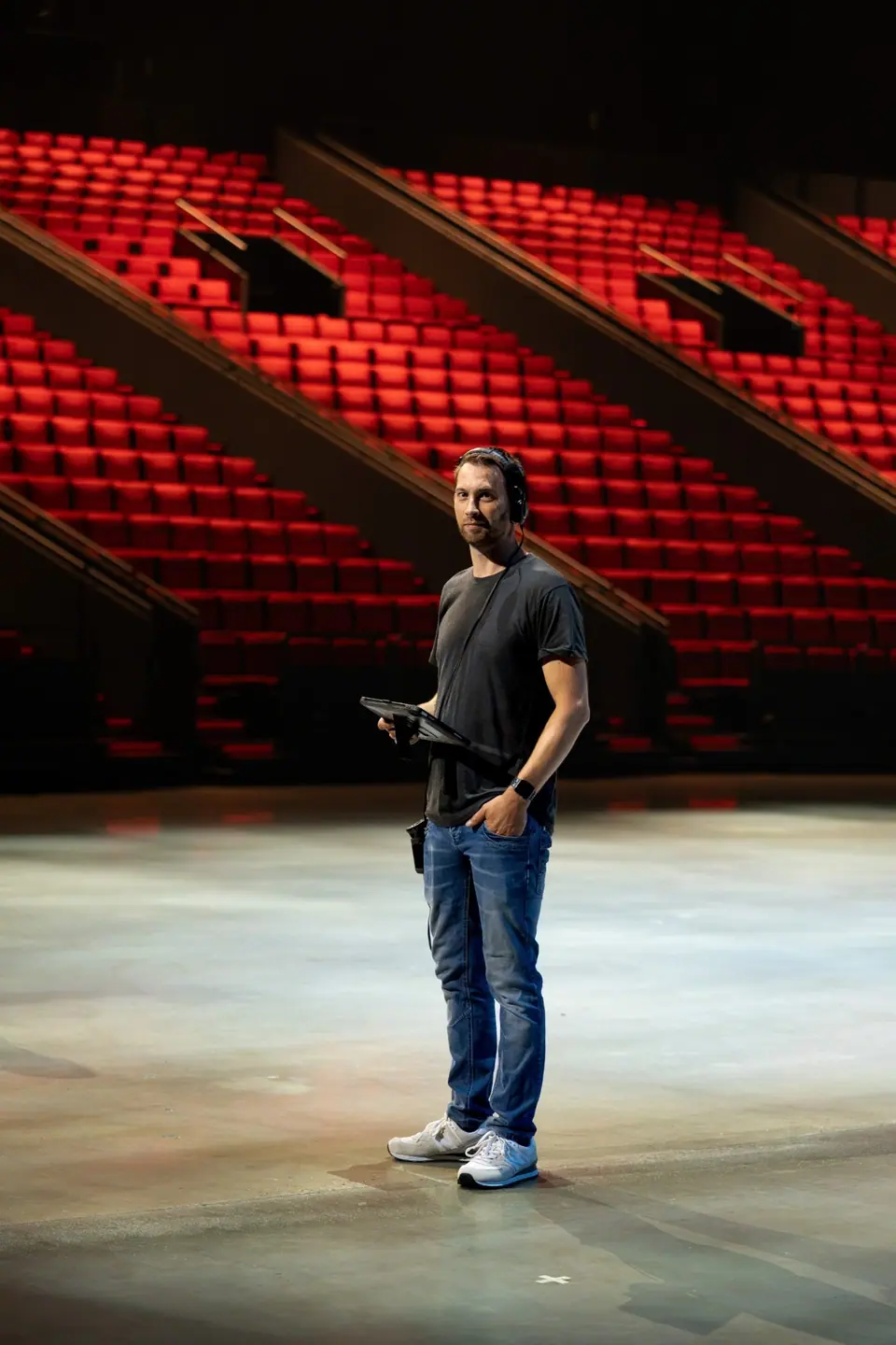 Paul Heijkens met headset en tablet op de vloer van een lege zaal met rode stoelen