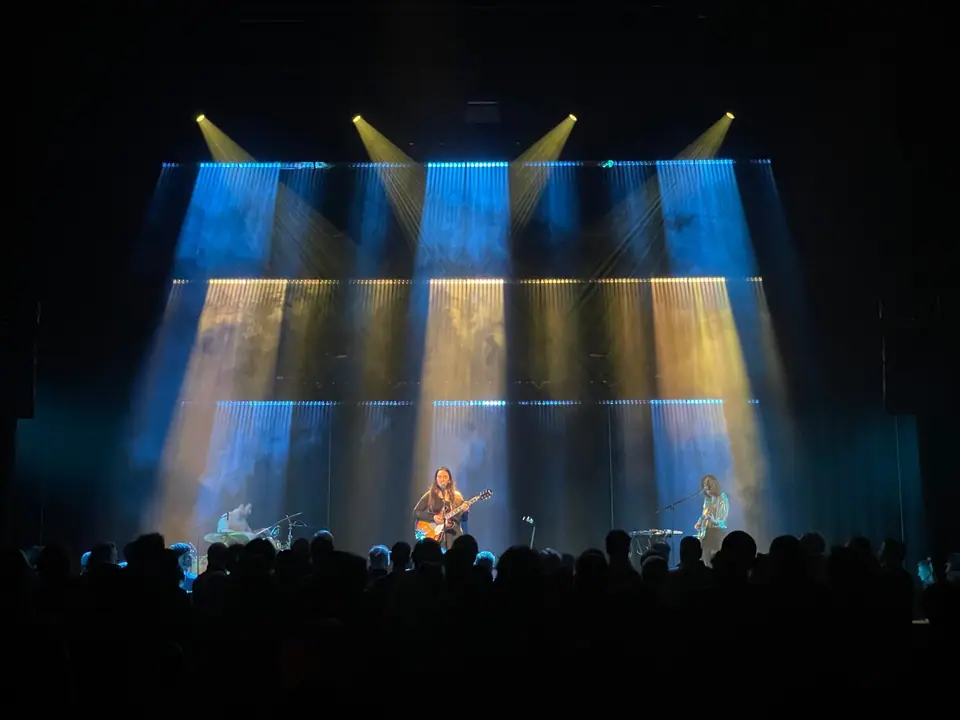 Rewire Festival 2026: zangeres met gitaar in blauw en geel licht, gekruiste spots erboven