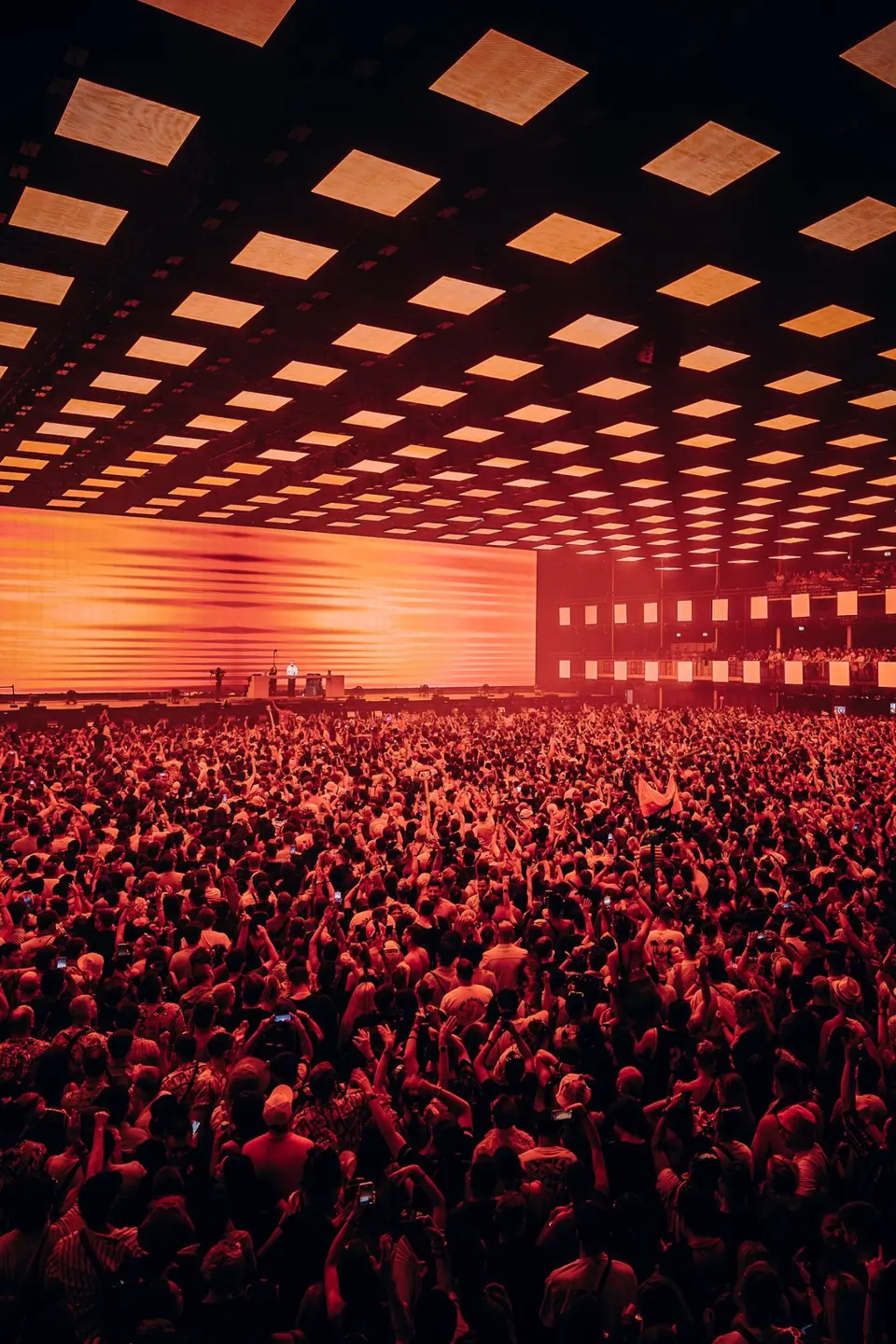 Tomorrowland 2025: oranje LED-plafond tot achter in de zaal, publiek met handen omhoog