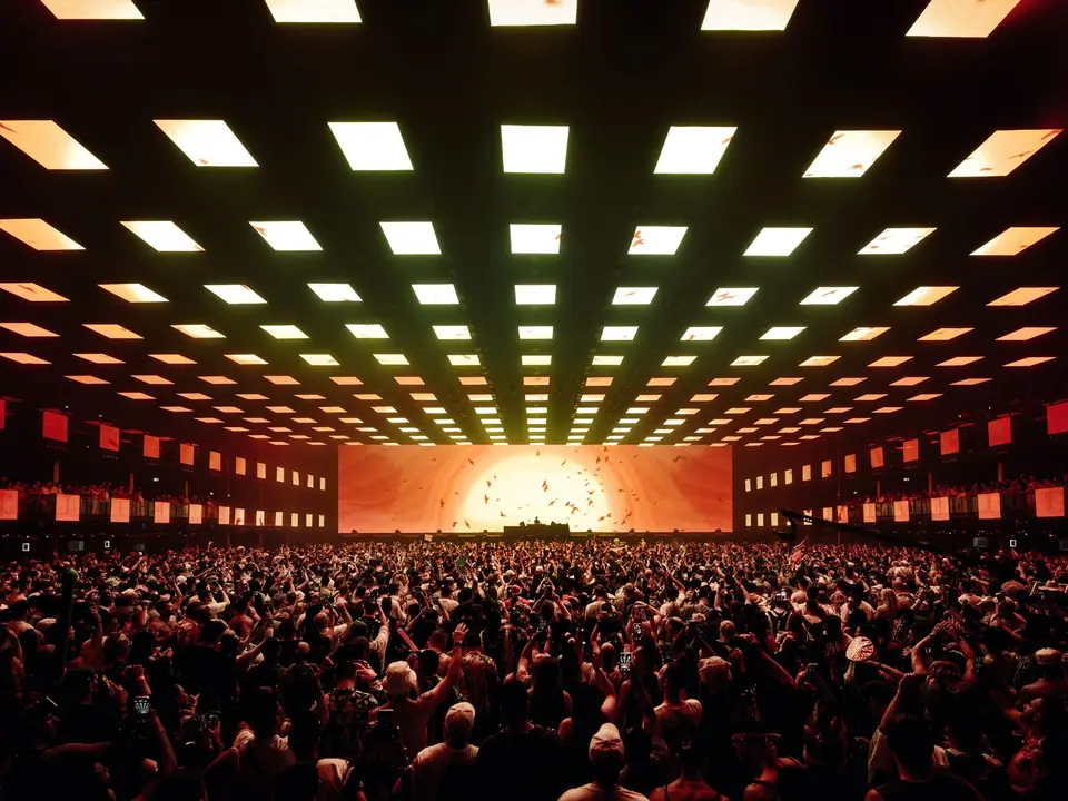 Tomorrowland 2025: plafond vol LED-schermen boven een volle zaal, op de achterwand een zon met vogels