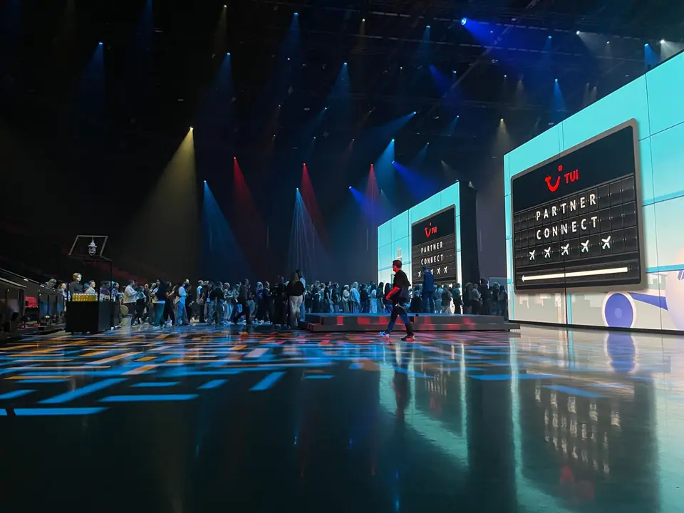 TUI Take Off 2026: publiek loopt de zaal in, beams in blauw, rood en geel boven LED-wanden met Partner Connect